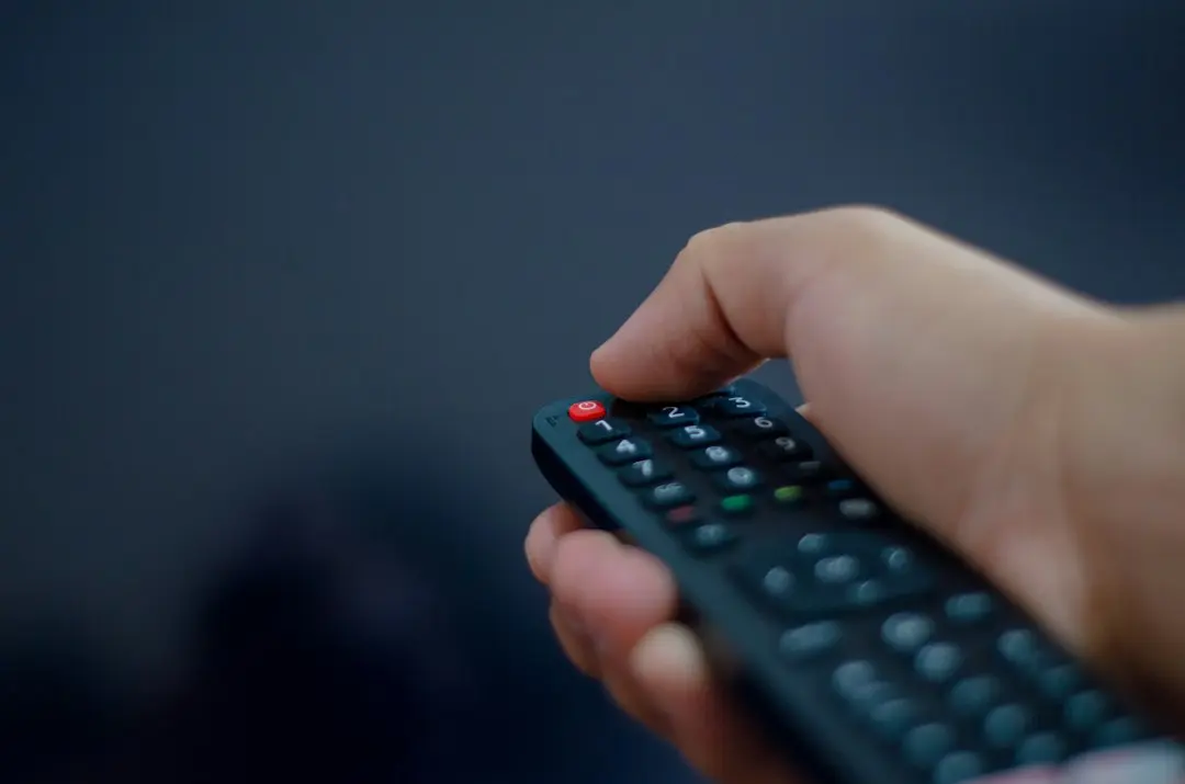 A hand pointing a TV remote control against a dark background, ready to sign in to IPTV Smarters Pro with a GaroxTV login