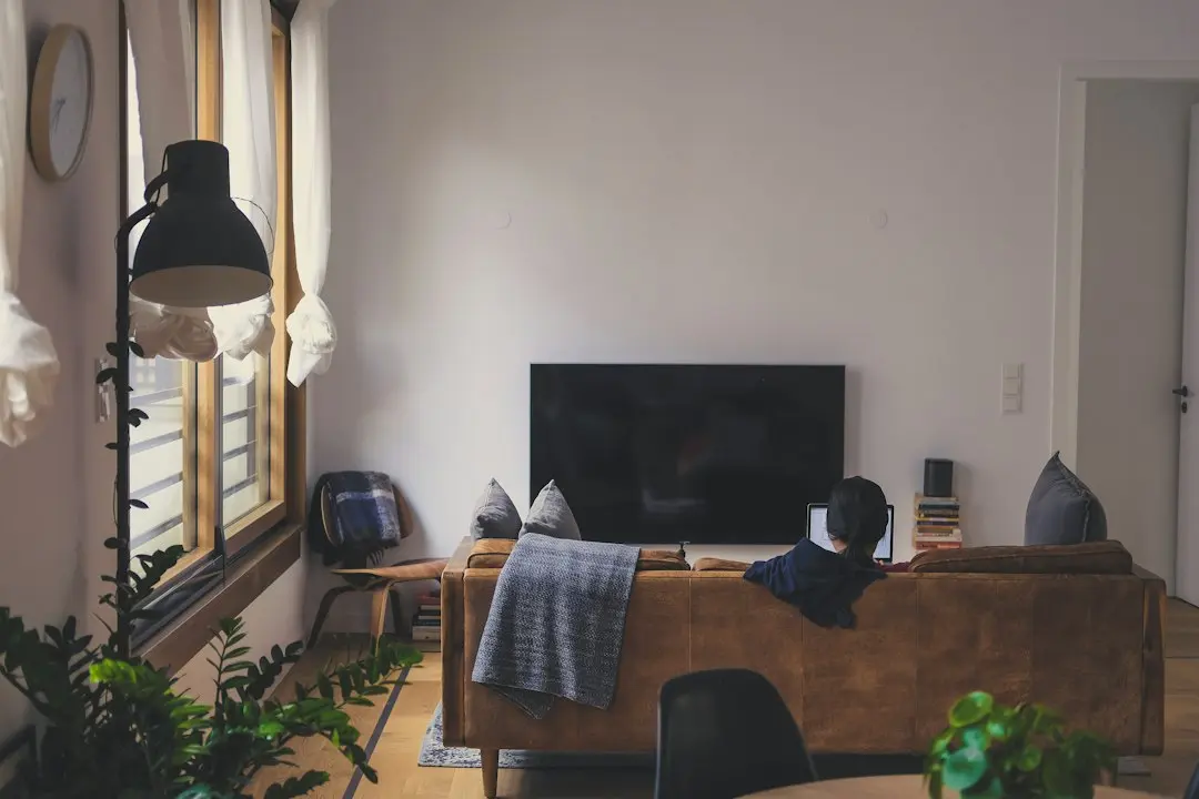 A person on a sofa facing a TV in a bright living room, the way a household settles in to watch live sports on GaroxTV
